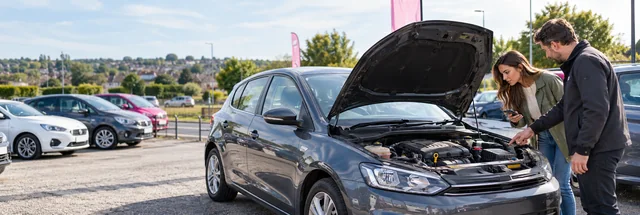 First-time buyer inspecting the engine of a used hatchback with a UK dealership adviser